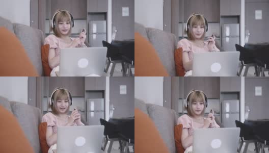 一个亚洲女人坐在沙发上，用笔记本电脑在家里学习电子学习高清在线视频素材下载