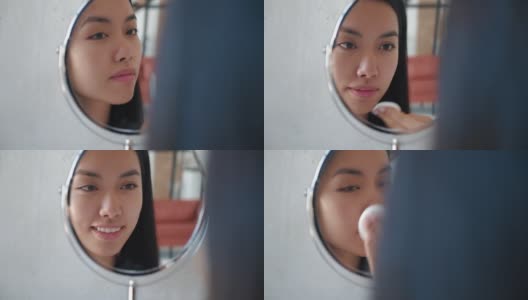 可爱美丽自然黑发的亚洲女孩用棉棉洗脸微笑着看着自己在化妆小镜中的倒影。美女用洁面乳和化妆棉卸妆高清在线视频素材下载