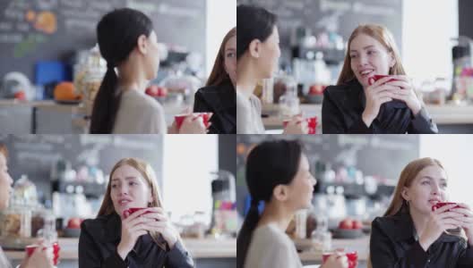 右图是两个年轻女人在咖啡馆喝茶或喝咖啡，愉快地聊天。红发白人女性聊天与分散的亚洲朋友高清在线视频素材下载