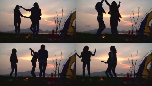 低角度的观点:朋友跳舞围绕篝火在夏天，而露营附近的湖在日落高清在线视频素材下载