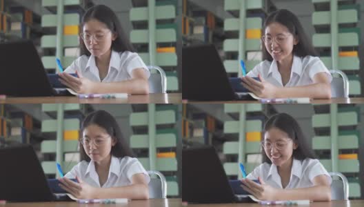 亚洲大学生女孩读书和工作用笔记本电脑和智能手机做她的家庭作业在公共图书馆高清在线视频素材下载