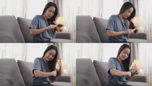 年轻的亚洲女子坐在家里客厅的沙发上梳头，是人们的生活方式发型师的概念。高清在线视频素材下载