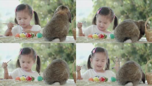 亚洲小女孩在复活节书桌上的兔子旁边给复活节蛋涂色。高清在线视频素材下载