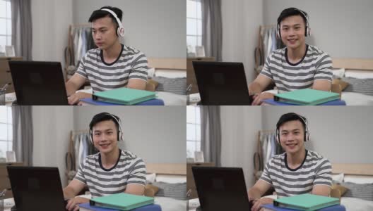 在封锁期间，戴着耳机的亚洲年轻男性在卧室里用笔记本电脑学习时，微笑着看着摄像头高清在线视频素材下载