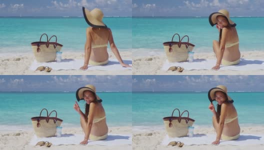女人在海滩度假看着相机微笑快乐放松在夏天的太阳日光浴浴巾在原始田园诗般的加勒比海滩，多种族亚洲/高加索女孩。缓慢的运动。高清在线视频素材下载