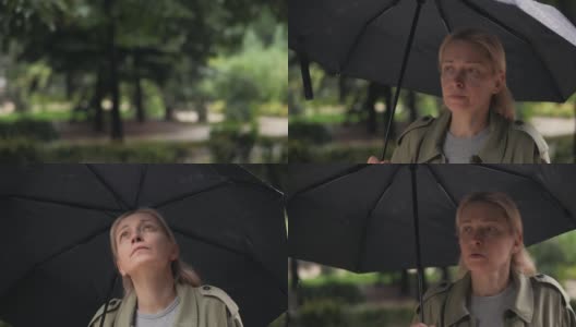 一个女人在雨中看着天空，等待雨的结束。高清在线视频素材下载