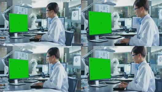 坐在办公桌前的亚洲科学家在一台模拟绿色屏幕的个人电脑上工作。在计算机科学研究实验室的机械臂模型。高清在线视频素材下载