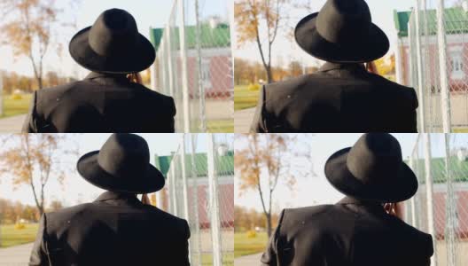 一个穿着黑色时髦西装，戴着帽子的年轻人走过去讲电话，特写，慢镜头高清在线视频素材下载
