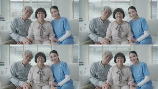 幸福的亚洲老年夫妇与在家庭护理坐在沙发微笑沙发看着相机与享受退休或隔离时间合影。亚洲老年人的生活方式。高清在线视频素材下载