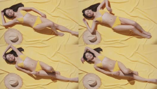 穿着比基尼的女人躺在黄色的沙滩毯上享受阳光高清在线视频素材下载