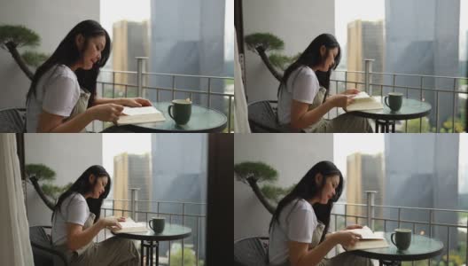 一个亚洲年轻女子在阳台上看书高清在线视频素材下载