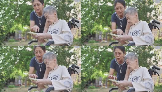 一位坐在轮椅上的残疾亚洲老人和她的年轻亚洲妇女在家里通过智能手机与家人进行视频聊天高清在线视频素材下载