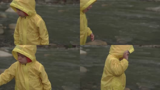 山区河流附近的学龄前儿童。穿黄色雨衣的小孩向河里扔石头。男孩把鹅卵石从岸上扔进水里。度假，去露营，春天，野性的自然，家庭观念高清在线视频素材下载