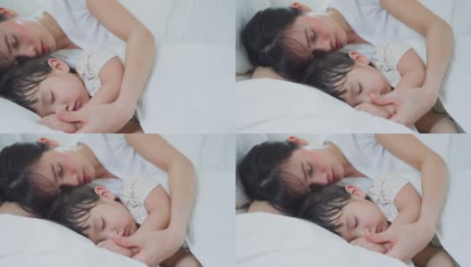 亚喜一家人待在家里，妈妈和女儿睡在卧室里。迷人的爱的父母，妈妈花时间和抱着熟睡的小女孩婴儿在床上的家早上。高清在线视频素材下载