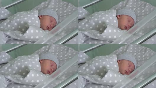 刚出生的婴儿红色可爱的脸肖像早期睡在灰色背景的医用玻璃床上。《帽子上生命开始的几分钟》中的孩子。婴儿，分娩，出生的最初时刻，开始的概念高清在线视频素材下载