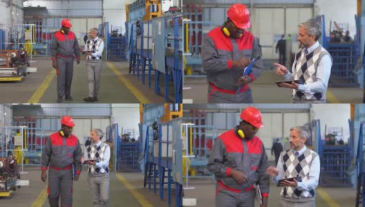 白人生产经理和黑人工人穿着防护工作服在工厂大厅里谈话和行走-放大镜头高清在线视频素材下载
