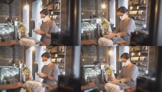 两名亚洲妇女戴着防护口罩在咖啡店用智能手机付款高清在线视频素材下载