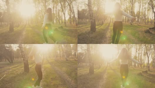 迷人的年轻女子穿着毛衣，牛仔裤在花苹果树跳舞和纺纱。夕阳，春天的果园和绿色的田野。缓慢的运动。高清在线视频素材下载