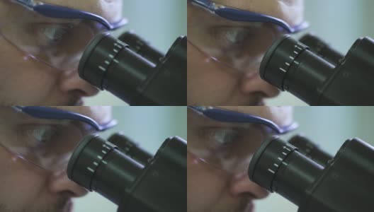 男性科学家戴着防护眼镜通过显微镜观察的特写镜头高清在线视频素材下载