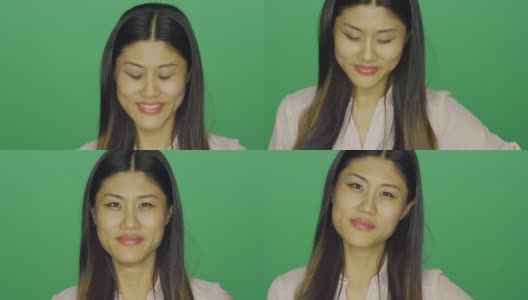 美丽的亚洲女人微笑和咯咯笑，在一个绿色屏幕的工作室背景高清在线视频素材下载