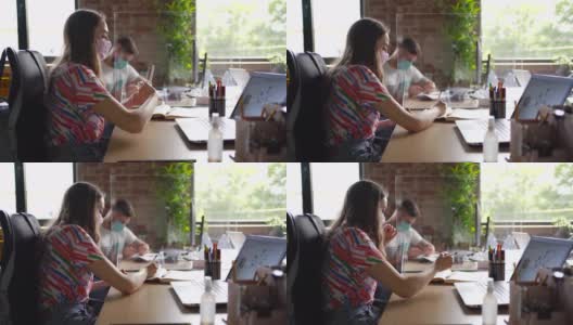 两个戴着口罩的商务人士在他们的办公桌前工作，他们之间有一个屏幕隔板高清在线视频素材下载