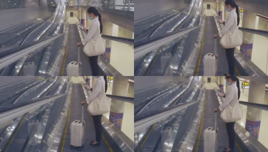 新冠肺炎疫情期间，亚洲游客佩戴医用口罩，在机场候机楼自动扶梯上使用智能手机，保持社交距离。高清在线视频素材下载