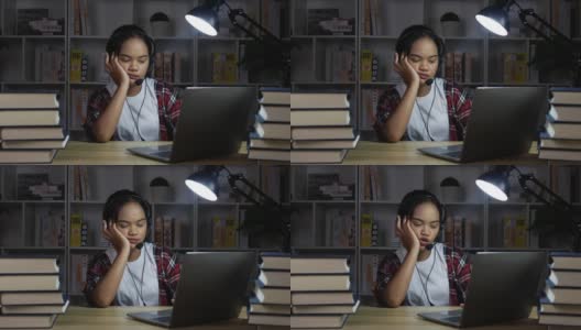 疲倦的女性戴着耳机和眼镜在晚上用笔记本电脑学习高清在线视频素材下载