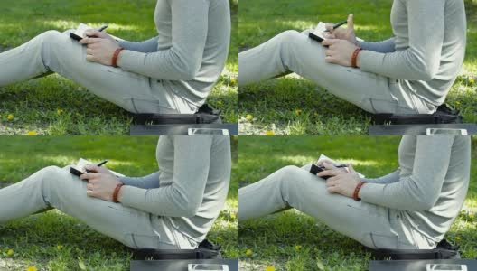 他坐在公园的草地上，在笔记本上写字高清在线视频素材下载
