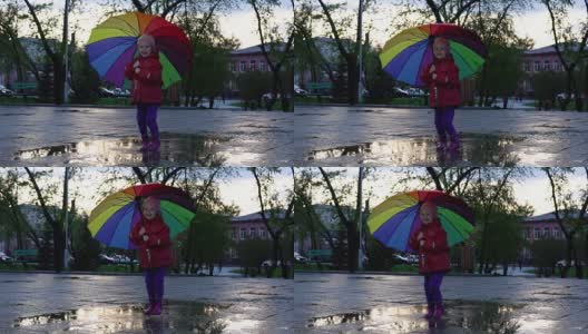 可爱的小女孩拿着五颜六色的雨伞在夕阳下的公园里的水坑里跳跃。高清在线视频素材下载