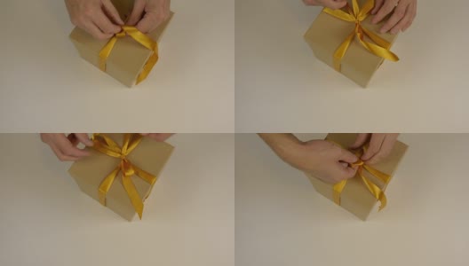 近上俯视图高角度。男人的手做蝴蝶结缎带在棕色纸盒礼盒。白色米色背景。为庆祝节日准备礼物。圣诞礼物盒子。高清在线视频素材下载