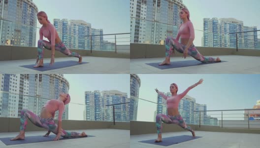 年轻苗条健康的女人，染着粉红色的头发，在摩天大楼的露台上做瑜伽练习和普拉提练习，在大都市中感觉平静。慢动作高清在线视频素材下载