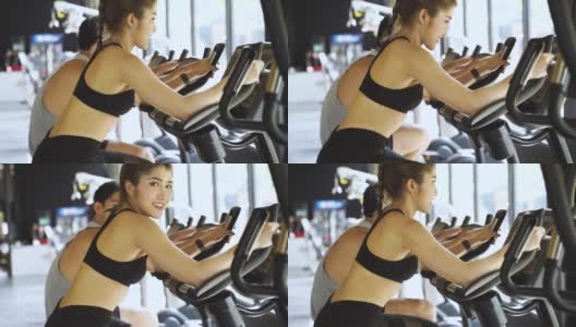 迷人的亚洲女人在健身房骑动感单车，看着镜头。健康和减肥的生活方式高清在线视频素材下载