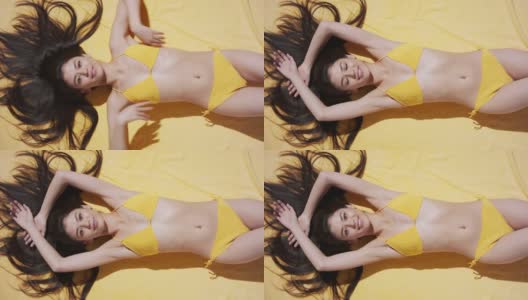 穿着比基尼的女人躺在黄色毯子上晒太阳，面带微笑高清在线视频素材下载