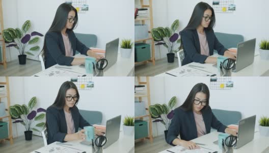 亚洲女员工穿着西装，在办公室用笔记本电脑工作，喝咖啡，看文件高清在线视频素材下载