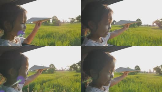 可爱的小女孩在乡下玩着玩具纸飞机窗外。晚上放松的活动概念。Slowmotion拍摄高清在线视频素材下载