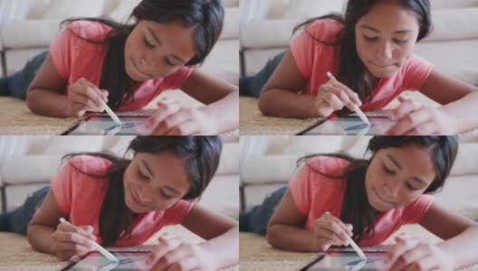 一个十几岁的女孩躺在客厅的地板上用着平板电脑和手写笔，特写高清在线视频素材下载