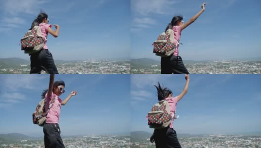 快乐的亚洲背包女孩戴着太阳镜，在山顶上对着蓝天跳舞，生活理念。高清在线视频素材下载
