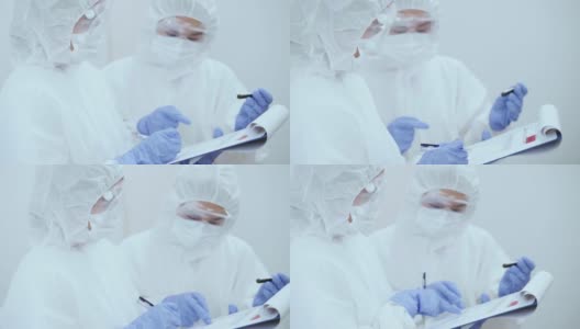 冠状病毒大流行期间，两名身穿防护服的医护人员在写字板上讨论血液检测结果。高清在线视频素材下载