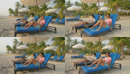 快乐的亚洲孩子戴着太阳镜在海滩椅上放松在早上在酒店或度假村度假，与家人，生活理念。高清在线视频素材下载