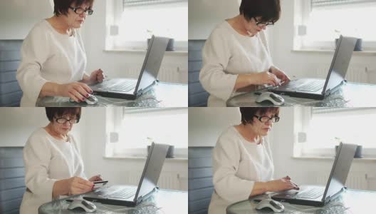一位上了年纪的妇女用笔记本电脑和银行卡付账。在线支付。远视高清在线视频素材下载