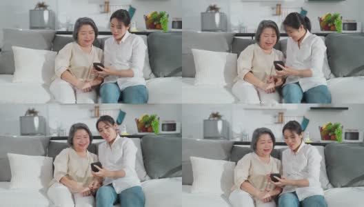 亚洲家庭妇女和她的母亲使用智能手机教玩互联网一起在客厅在家里的幸福和微笑。两代沟技术使用生活方式的概念。高清在线视频素材下载