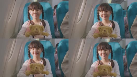 亚洲小女孩拥抱熊娃娃的肖像，坐在飞机上。孩子感到兴奋和快乐的旅行与她的家人。乘客在飞机上的运输概念。高清在线视频素材下载