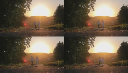年轻夫妇手牵着手在夕阳下散步。一对相爱的情侣在夕阳下的公园散步。橙色的日落高清在线视频素材下载