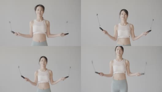 可爱的韩国女性跳绳在白色的工作室，穿着紧身裤和运动背心，精力充沛健康的女性高清在线视频素材下载
