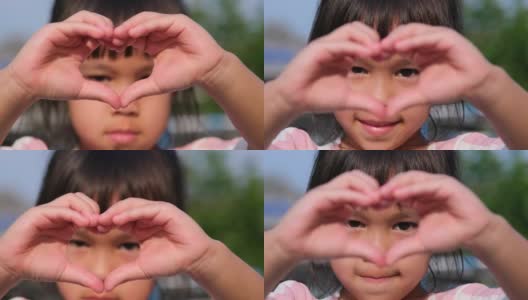 一个亚洲小女孩的特写镜头，看着相机，用她的手做一个心形。心形象征着爱。高清在线视频素材下载