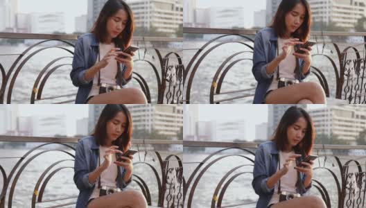 亚洲女性使用智能手机与她的朋友聊天，而坐在湄南河在泰国在美丽的日落。高清在线视频素材下载