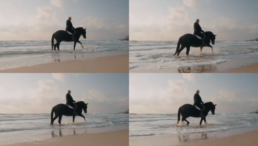 一位短发的中年妇女在海边小心翼翼地骑着黑马。缓慢的运动。海滩上的秋日日出或日落。美丽的景色高清在线视频素材下载
