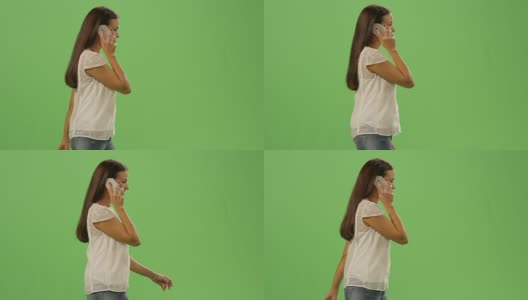 随便的年轻褐发女孩正在走路和讲电话在一个模拟的绿色屏幕在背景。高清在线视频素材下载