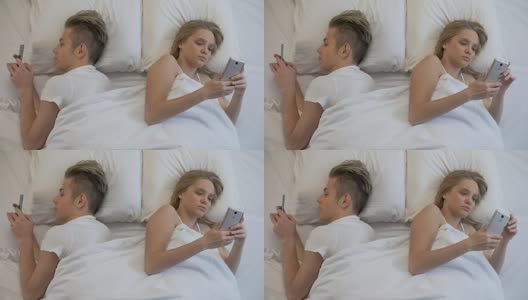 夫妻背靠背躺在床上玩着智能手机，玩着社交网络，视而不见高清在线视频素材下载
