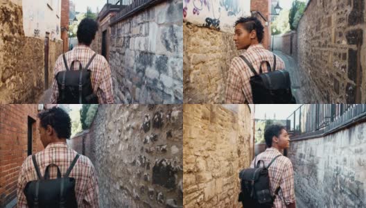 年轻的黑人妇女背着背包走在石头墙之间的狭窄小巷里，后视镜，跟着开枪高清在线视频素材下载
